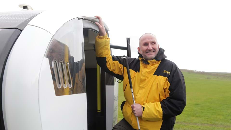 Blind veteran Mark holding a guide cane as he enters a driverless pod