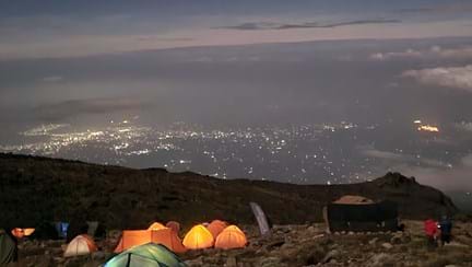 A selection of tents all glowing due to torch lights inside, high on the side of the mountain