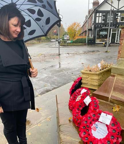 Sharon holds an umbrella as she stands looking at the wreath she has laid