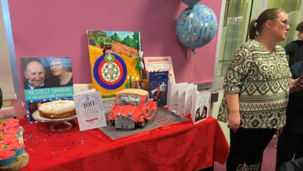 A table displaying a birthday cake, cards and balloons at blind veteran Ken's 100th birthday