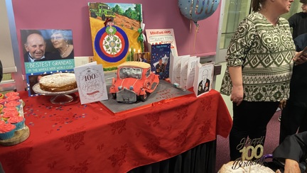 A table displaying a birthday cake, cards and balloons at blind veteran Ken's 100th birthday