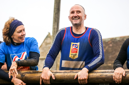 A group of four runners in Blind Veterans UK vests, muddy and smiling as they rest after they finished their race