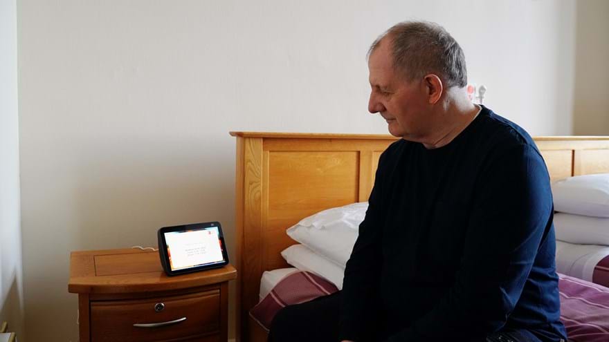 A blind veteran sitting on the edge of a bed using the Alexa system in Llandudno