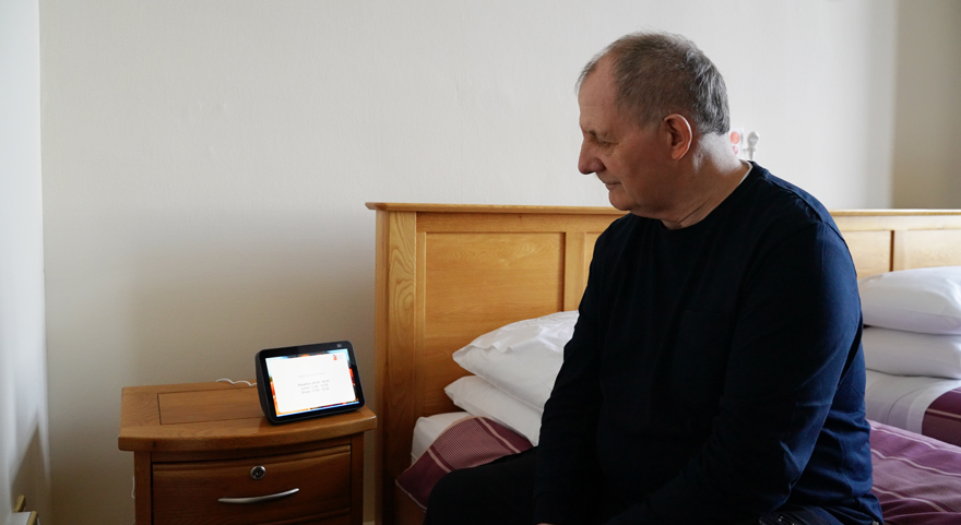 A blind veteran sitting on the edge of a bed using the Alexa system in Llandudno