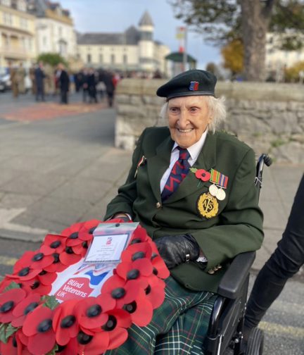 Blind veteran Margaret wearing her military badges and beret, holding a poppy wreath