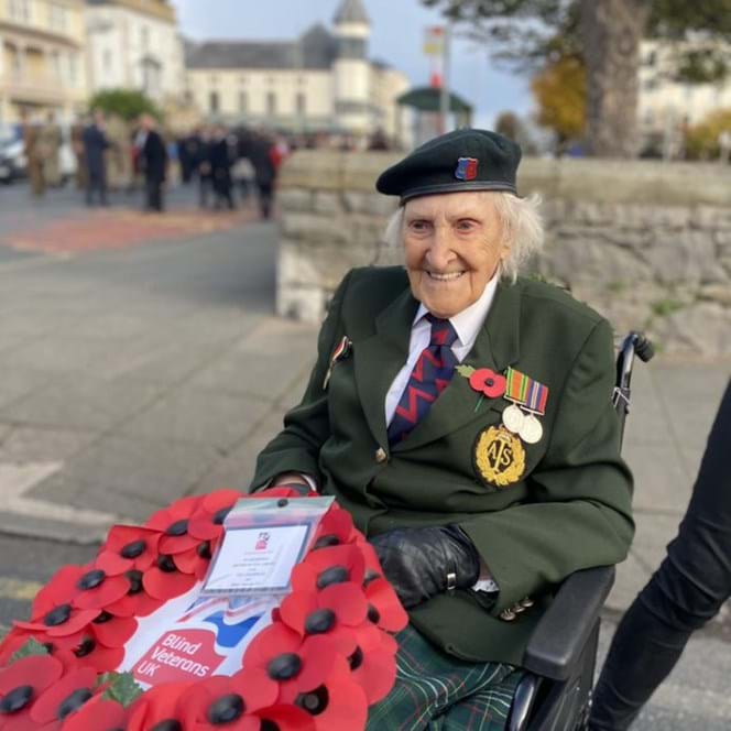 Blind veteran Margaret wearing her military badges and beret, holding a poppy wreath