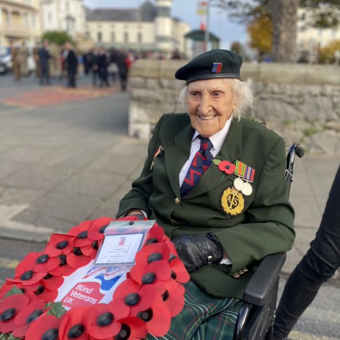 Blind veteran Margaret wearing her military badges and beret, holding a poppy wreath