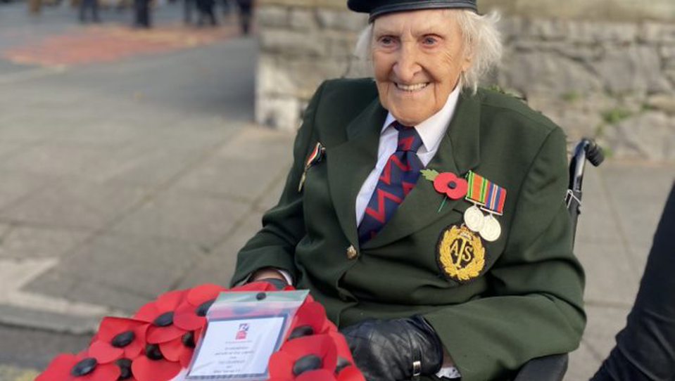 Blind veteran Margaret wearing her military badges and beret, holding a poppy wreath