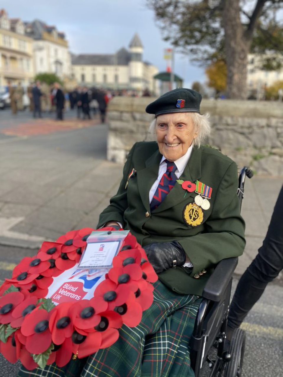 Blind veteran Margaret wearing her military badges and beret, holding a poppy wreath