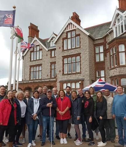 Group shot of Thea Pharmaceuticals team members with blind veteran Billy and Wellbeing Specialist Karla out side Blind Veterans UK's Llandudno Centre of Wellbeing