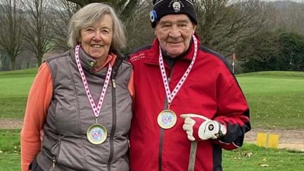 Danny and his wife standing side by side on the golf course with medals around their necks