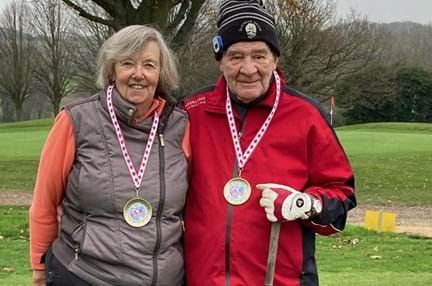 Danny and his wife standing side by side on the golf course with medals around their necks