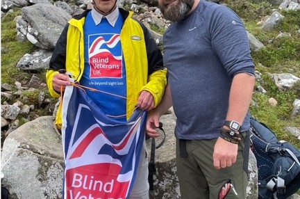 Volunteer Chris and blind veteran Pete pictured at the highest point reached on Ben Nevis, waving a Blind Veterans UK flag