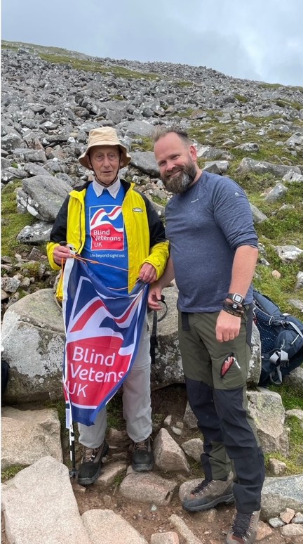 Volunteer Chris and blind veteran Pete pictured at the highest point reached on Ben Nevis, waving a Blind Veterans UK flag