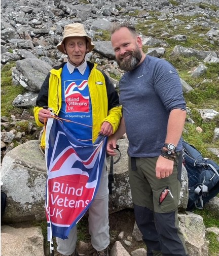 Volunteer Chris and blind veteran Pete pictured at the highest point reached on Ben Nevis, waving a Blind Veterans UK flag