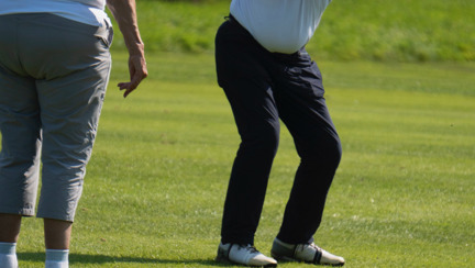 Danny mid swing with his golf club while his wife stands nearby as his guide