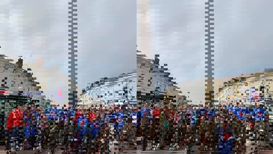 Group of walkers, some in Blind Veterans UK T-shirts, some in military themed costumes, gathered in front of Llandudno War Memorial.