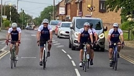 Five cyclists riding along next to each other across the width of the road 