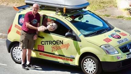 Supporter stood shaking hands with a large soft toy monkey sat in the driver's seat of his Citroen car