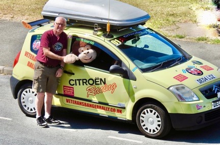 Supporter stood shaking hands with a large soft toy monkey sat in the driver's seat of his Citroen car