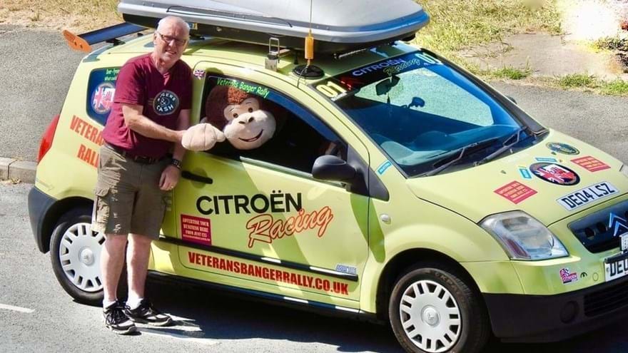 Supporter stood shaking hands with a large soft toy monkey sat in the driver's seat of his Citroen car