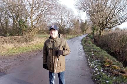 Blind veteran Brian walking along a path with a white cane