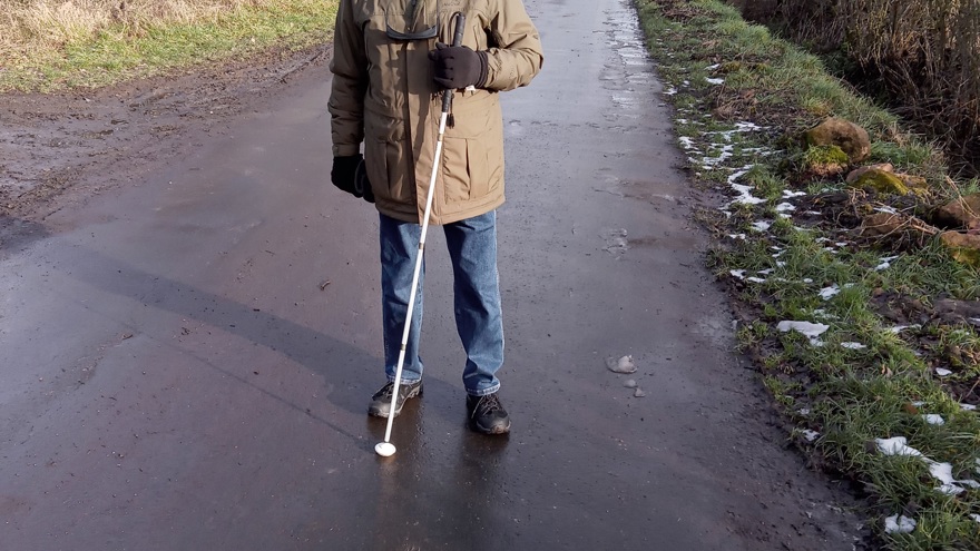 Blind veteran Brian walking along a path with a white cane