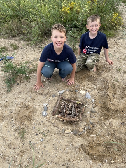 Sammy and Oakley knelt down behind the fire they have prepared but not yet lit