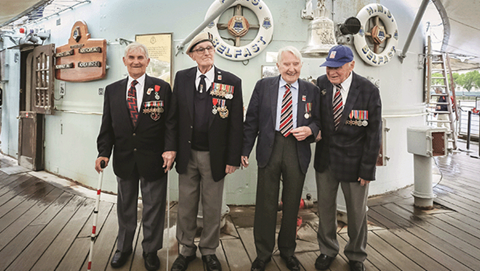 Four blind veterans, wearing their military badges and standing together, smiling and laughing