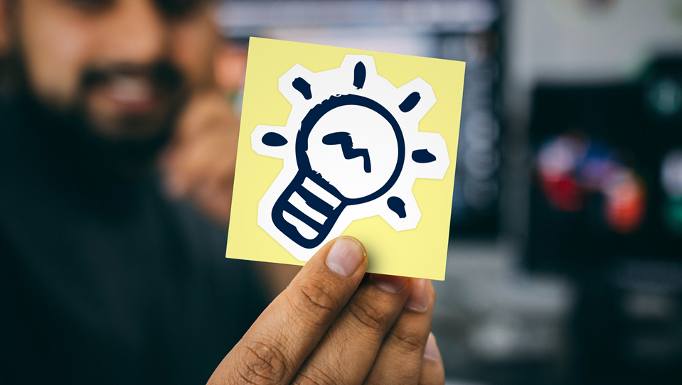 A photo of a man holding a sticky note with a light bulb on it
