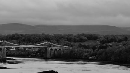 A black and white photograph of the Menai Bridge across the water