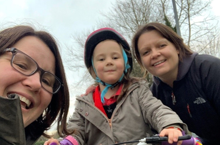 Photo of Kelly Ganfield, right, smiling with wife Sarah, left, and young daughter Bethany on trike, centre