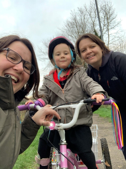 Photo of Kelly Ganfield, right, smiling with wife Sarah, left, and young daughter Bethany on trike, centre