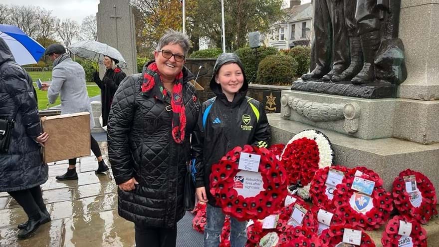 Sian stood with her grandson who is holding a poppy wreath stood next to the memorial where a number of wreaths have already been laid