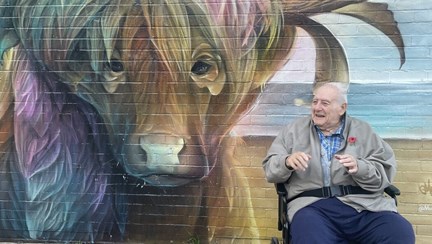 Blind veteran Maurice is in his wheelchair next to a large mural of a buffalo