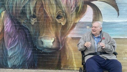 Blind veteran Maurice is in his wheelchair next to a large mural of a buffalo