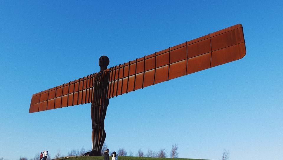 The Angel of the North statue, a large steel sculpture with wide spanning wings, placed on a grassy hill.