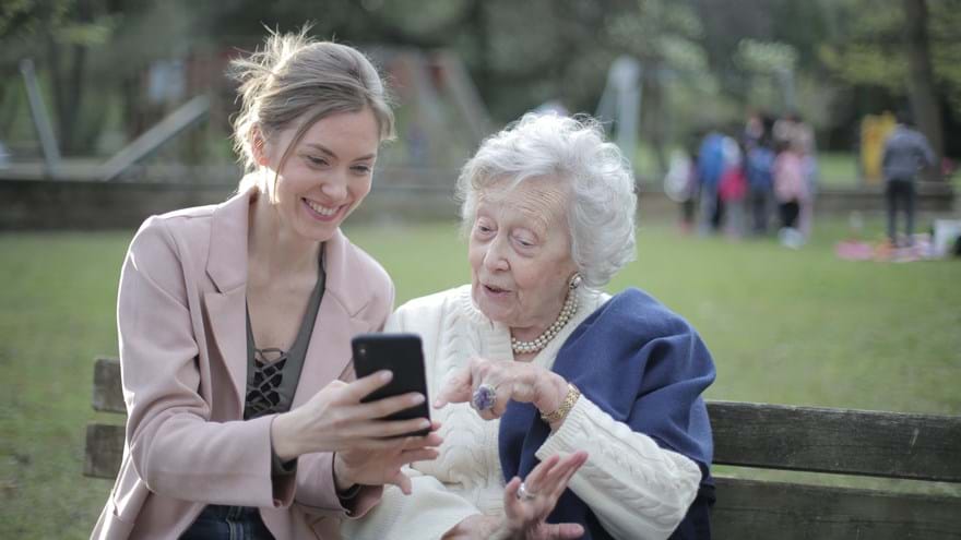 Older woman and daughter using a smart phone and sitting on a bench outside