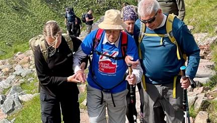Blind veteran Peter being guided and supported up a rocky part of the mountain by his family and fellow climbers