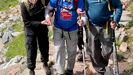 Blind veteran Peter being guided and supported up a rocky part of the mountain by his family and fellow climbers