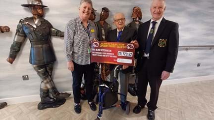Blind veteran Les is stood between Lesley and his son Keven as they present Lesley with a large cheque