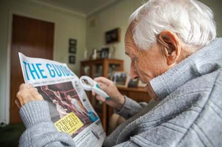 A photo of blind veteran Ron Cross using a magnifier to read The Guide newspaper at home