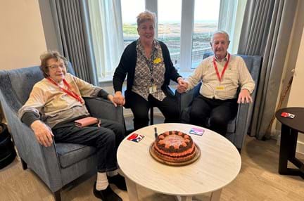 Terry, Joyce and Lesley are sat behind a cake that was baked to welcome the couple back to Rustington