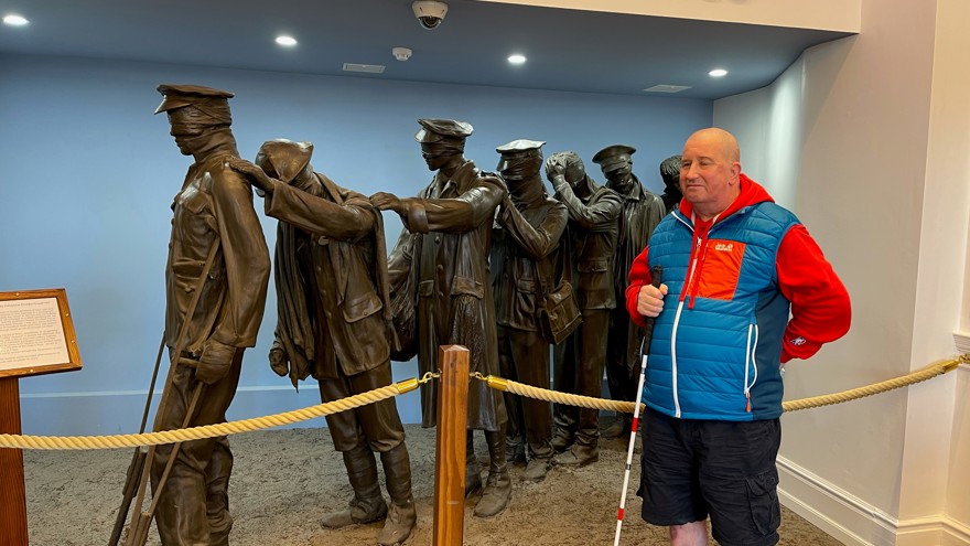 Blind veteran John standing with his white cane, in front of our Victory Over Blindness statue