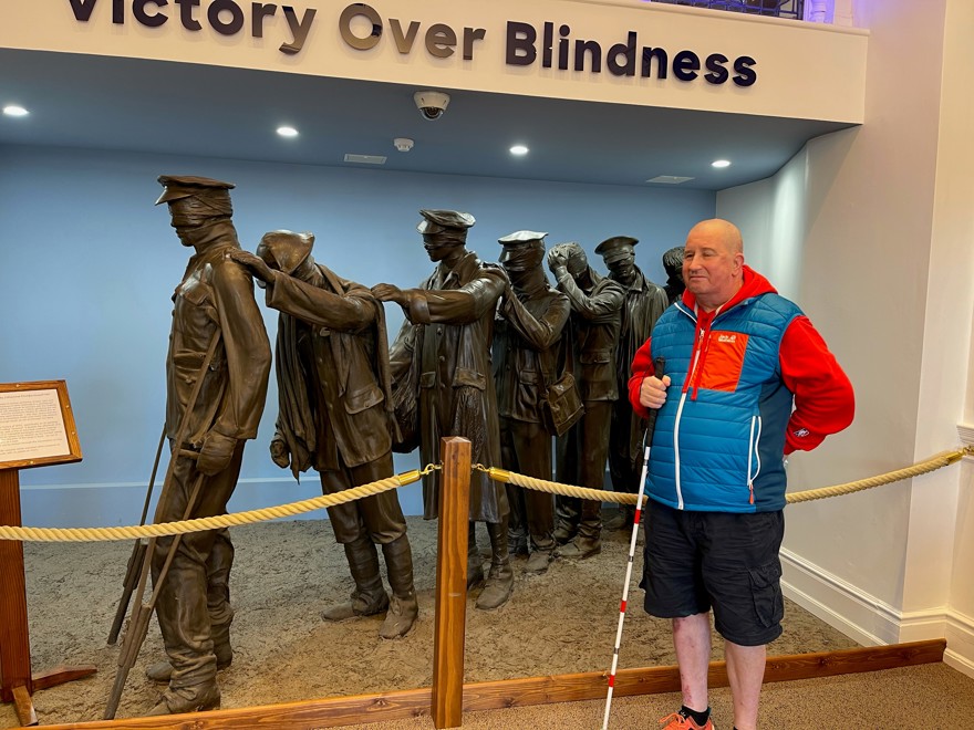 Blind veteran John standing with his white cane, in front of our Victory Over Blindness statue
