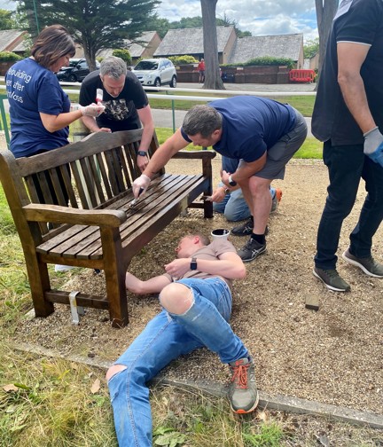 Four Thea colleagues working together to varnish a wooden garden bench at our Blind Veterans UK Llandudno Centre of Wellbeing.  One of the group is lay on the floor so he can reach underneath.