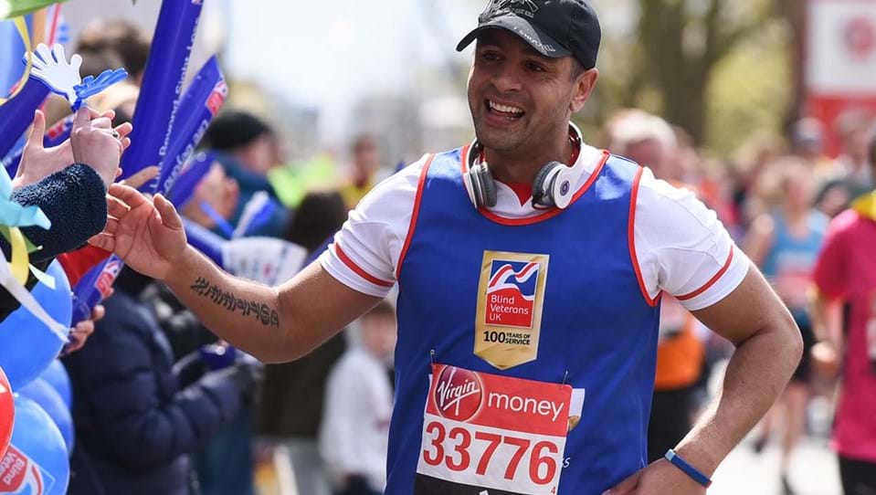 Charity supporter Dominic smiling as he runs along a crowd, wearing a Blind Veterans UK vest and holding his hand out to wave as he passes