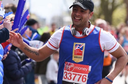 Charity supporter Dominic smiling as he runs along a crowd, wearing a Blind Veterans UK vest and holding his hand out to wave as he passes