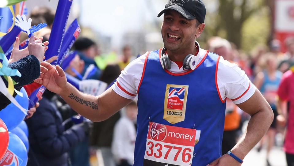 Charity supporter Dominic smiling as he runs along a crowd, wearing a Blind Veterans UK vest and holding his hand out to wave as he passes