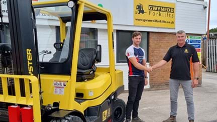 James stood in front of a forklift truck wearing his Blind Veterans UK t shirt shaking hands with his dad who is director of Gwynedd Forklifts Ltd